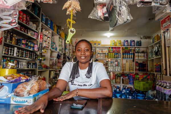 Shop owner at the counter of her fully stocked provisions store, phone beside her