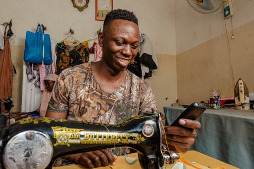 a man smiles as he uses a sewing machine