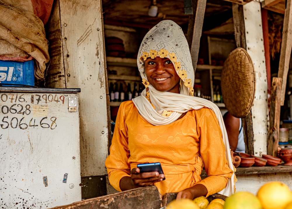 a woman standing in front of a fruit stand holding a cell phone