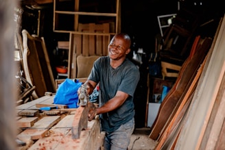 a man smiles as he works on a piece of wood