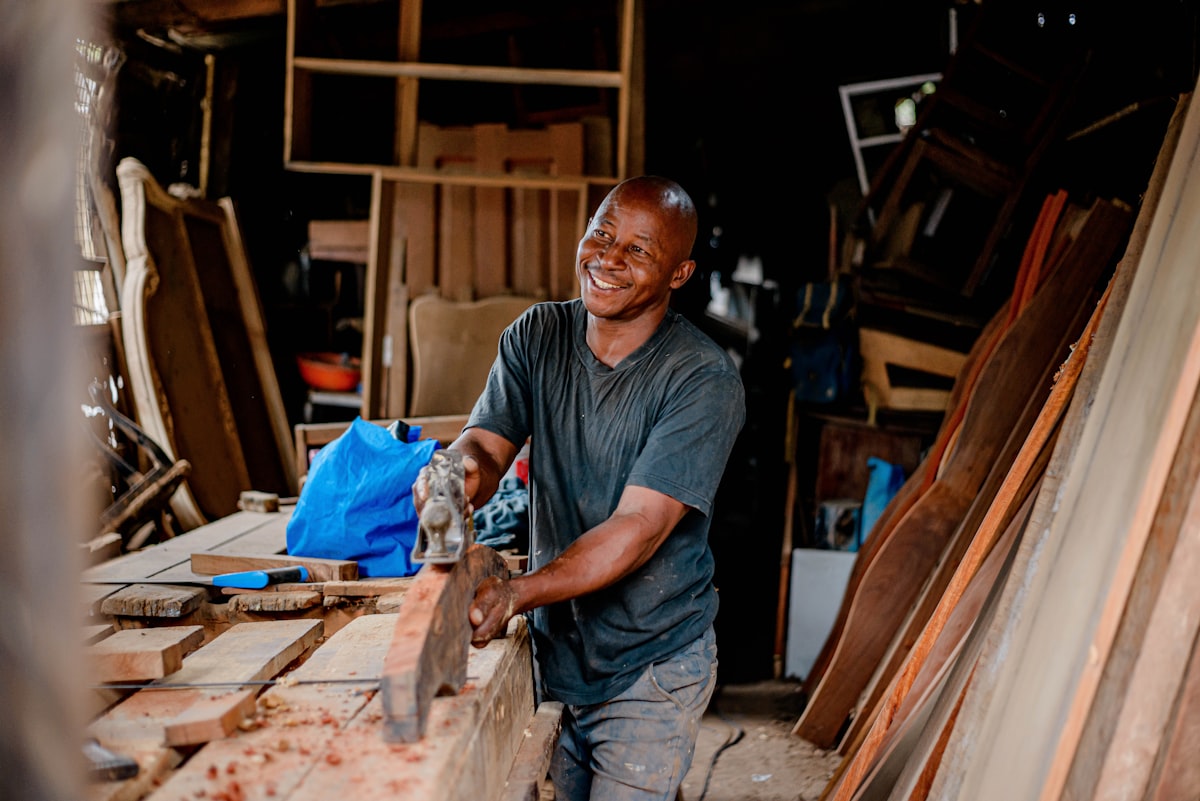 A small business owner smiling while working with his hands on a piece of wood in his shop, representing the makers and founders competing for federal small business grants this fall