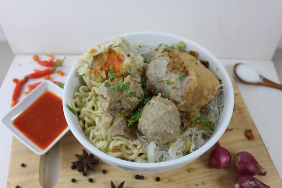 A bowl of steaming noodles topped with meatballs and herbs.