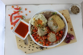 a bowl of food on a cutting board next to a bowl of sauce