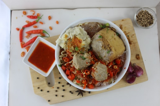 a bowl of food on a cutting board next to a bowl of sauce