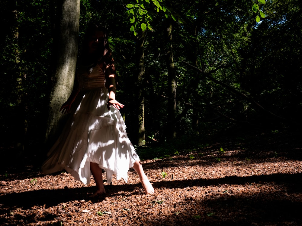 a woman in a white dress walking through a forest