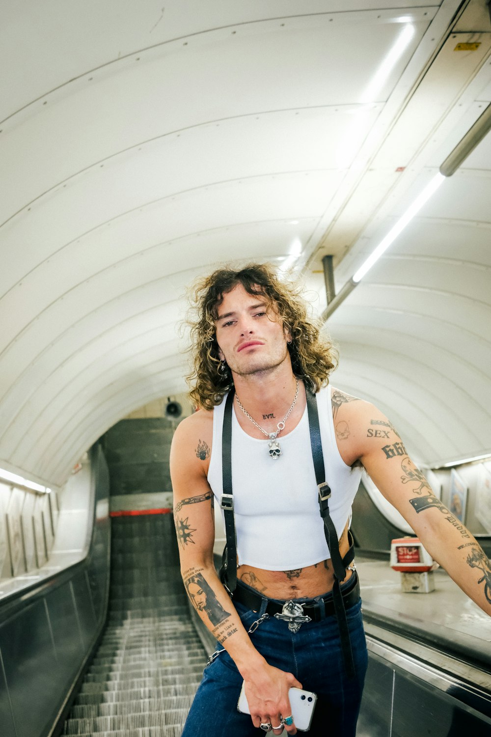 a man with long hair and tattoos standing on an escalator