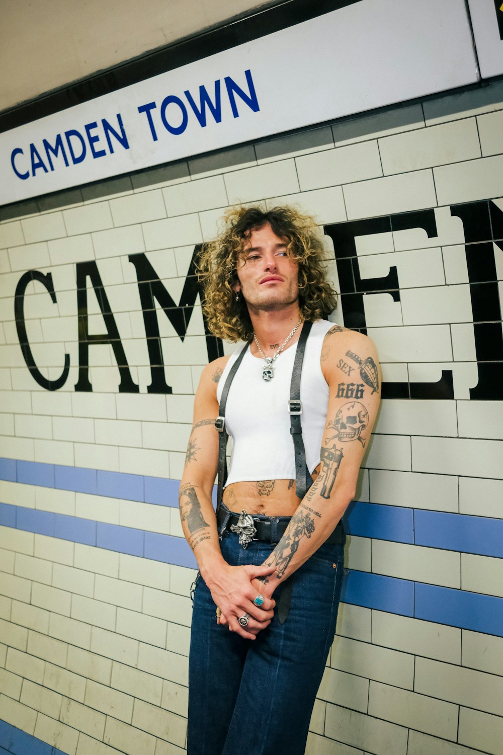 a man with tattoos standing in front of a sign