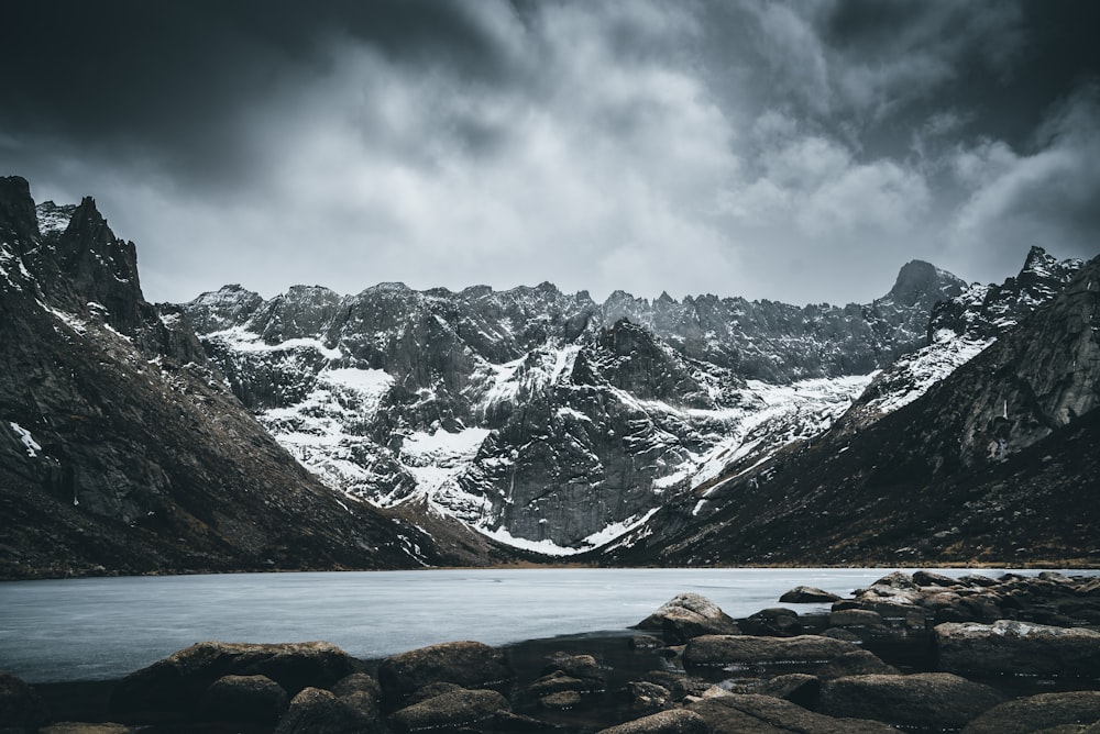 a lake surrounded by mountains under a cloudy sky