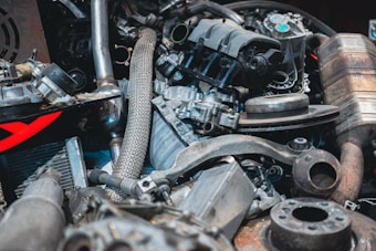 A jumble of various metal car parts, including pipes, gears, and engine components. The pieces are tightly packed together, with some showing signs of rust and wear, while others appear more polished. The image conveys a sense of complexity and mechanical intricacy.