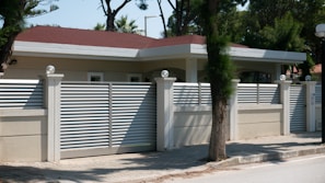 A sleek dark gray metal fence bordering a modern home with lush green landscaping
