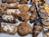 A variety of freshly baked pastries are displayed on trays, including croissants, chocolate-dipped palmiers, almond-topped pastries, and spiral cinnamon rolls. Price tags indicate the cost of some items.