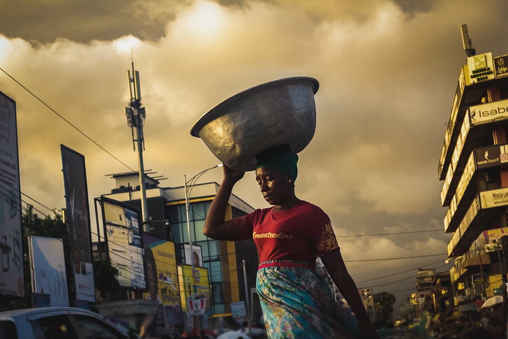 a woman carrying a large metal bowl on her head