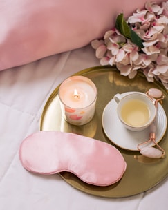 A stylish satin eye mask folded beside a vase of fresh flowers on a bedside table.