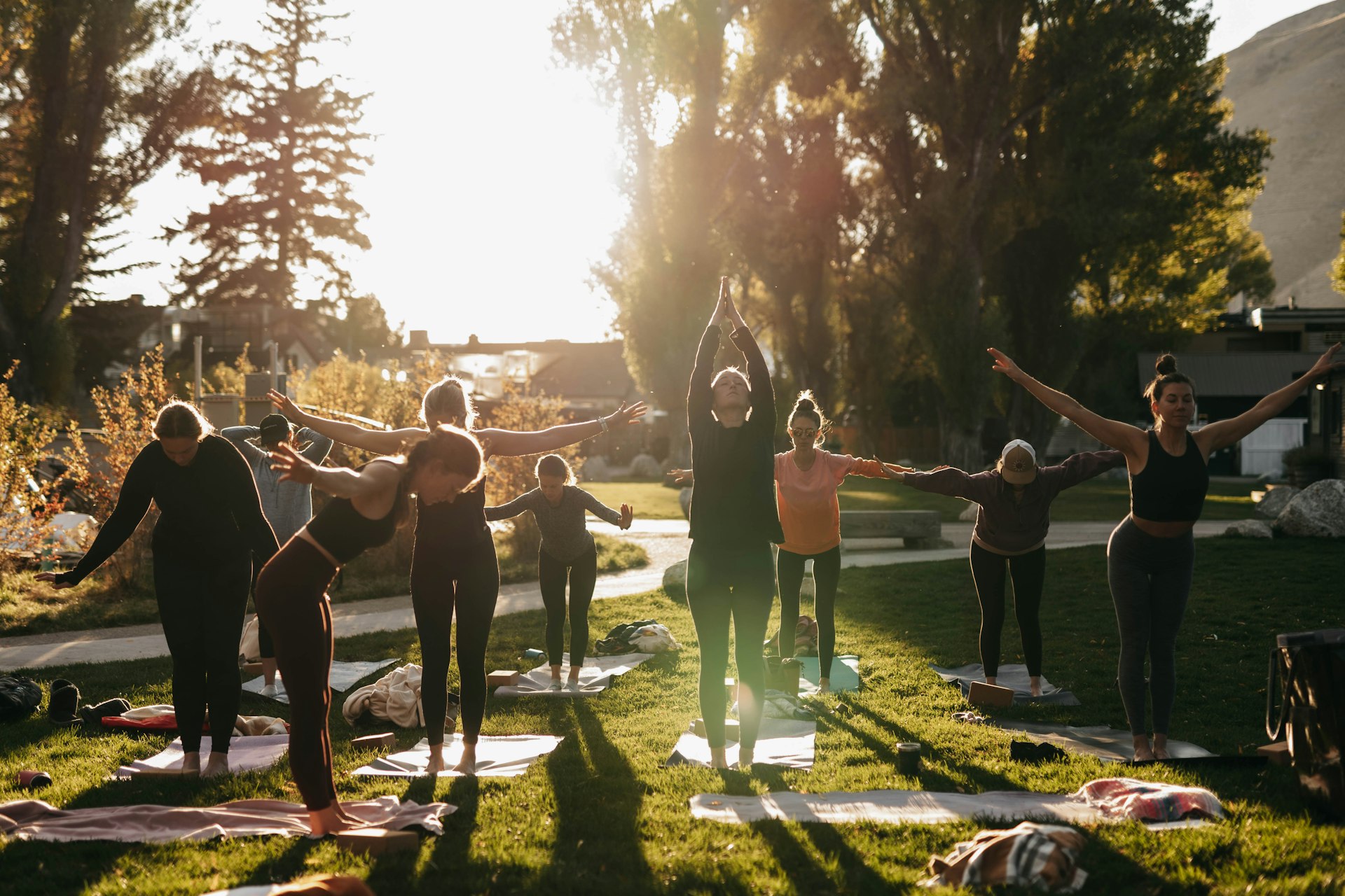 Group practicing yoga on mats in a park at sunset