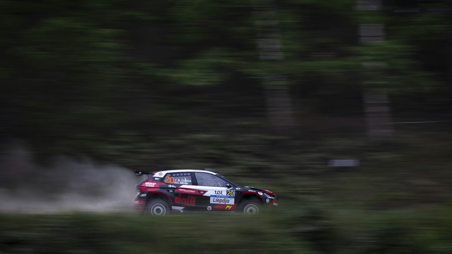 A dynamic shot of Sébastien Ogier’s rally car speeding through a forested section, sunlight filtering through the trees.