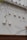 A series of white ventilation covers or fixtures are mounted on an exterior wall. The wall is made of light-colored material, and there are branches with sparse leaves in the foreground.