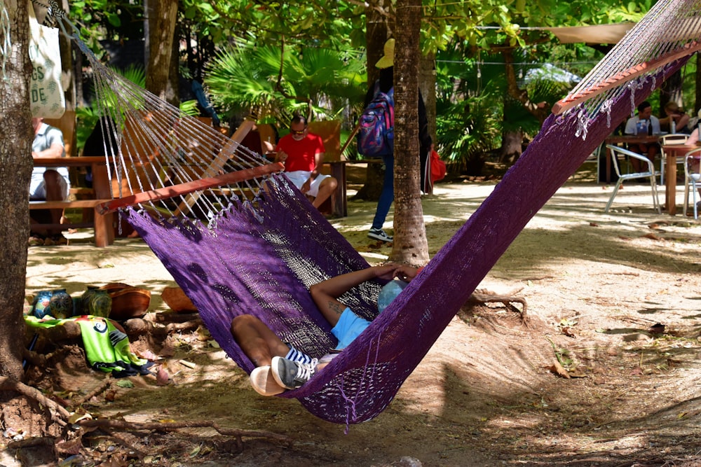 a man laying in a purple hammock in the shade