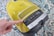 A yellow vacuum cleaner with a control panel featuring various icons for settings. A finger is pressing a button on the panel. The vacuum is placed on a patterned carpet with shades of blue, white, and black.
