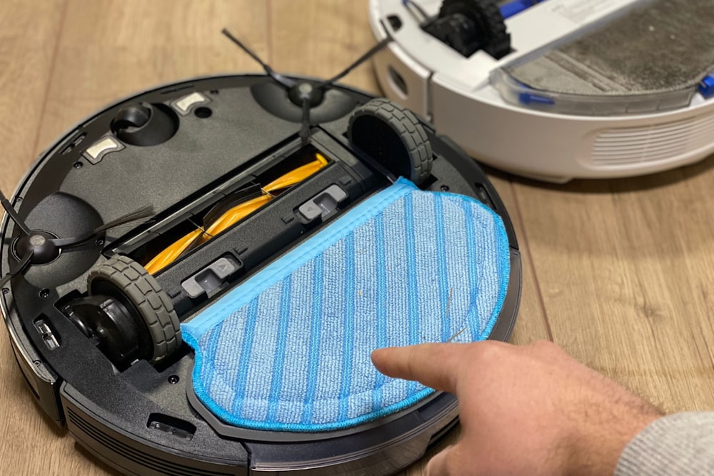 a person is holding a blue duster in front of a robot vacuum