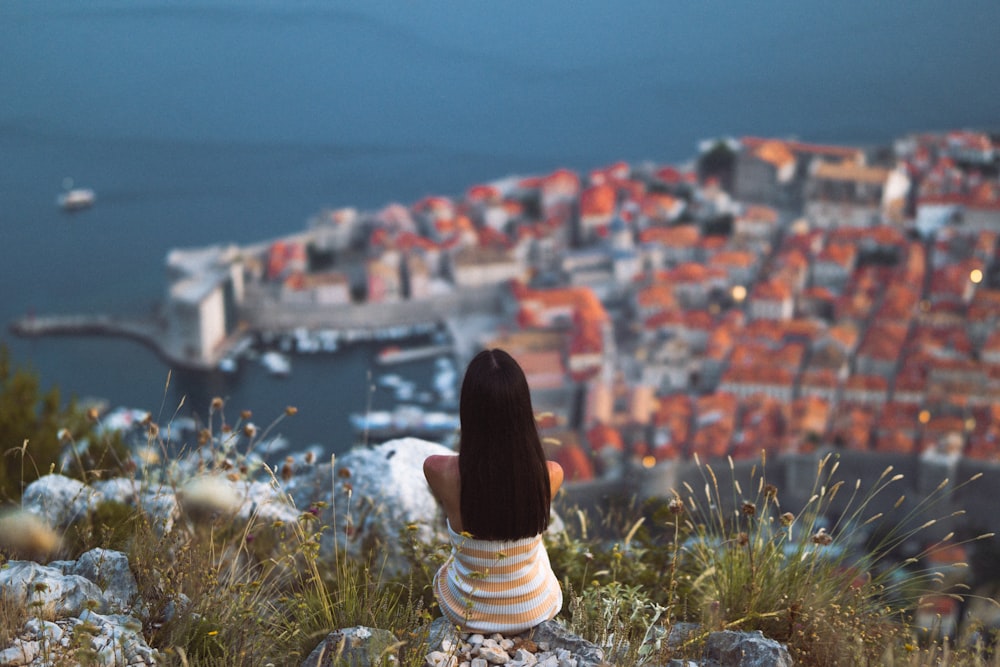 a woman sitting on top of a hill overlooking a city