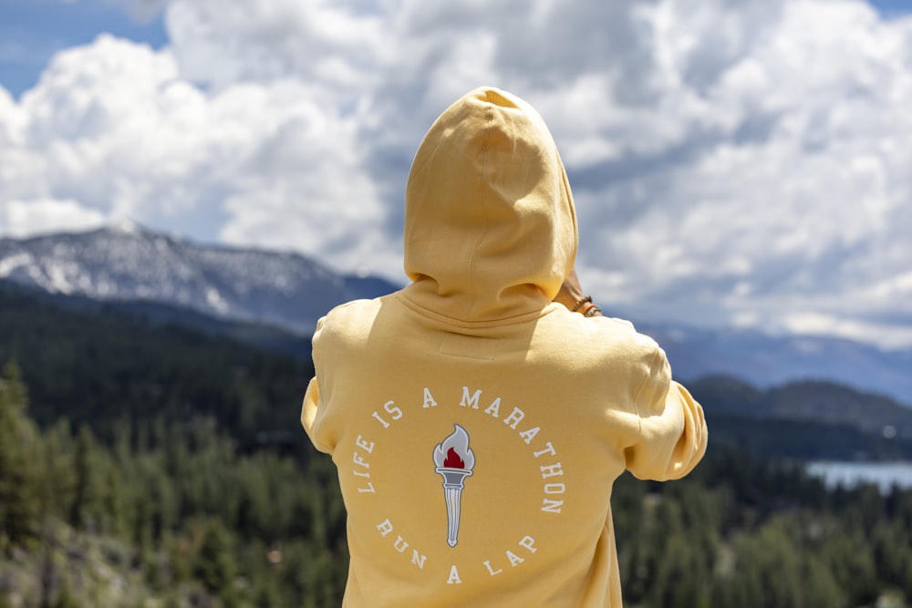 a person wearing a yellow hoodie looking out over a mountain