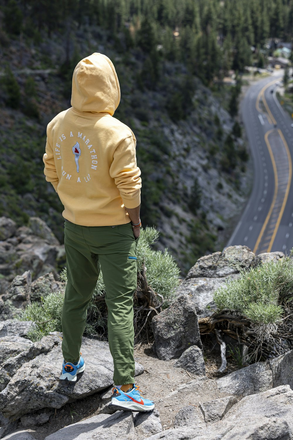 a person in a yellow hoodie standing on a rock