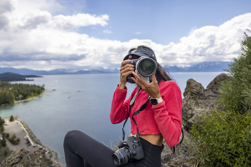 a woman taking a picture of a lake with a camera