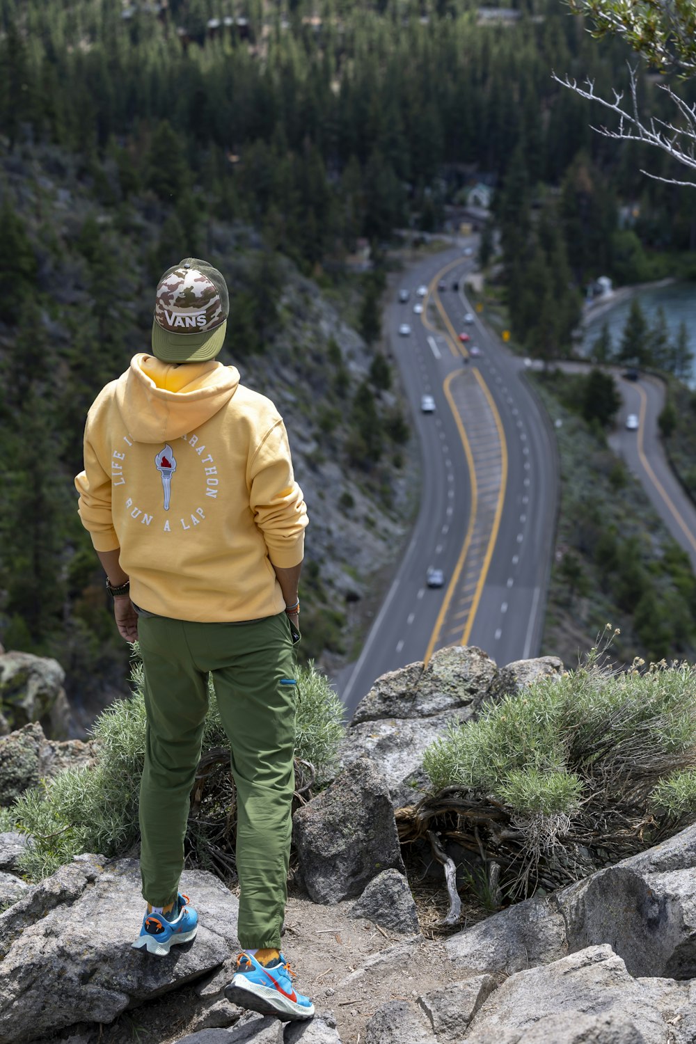 a man in a yellow hoodie is standing on a rock