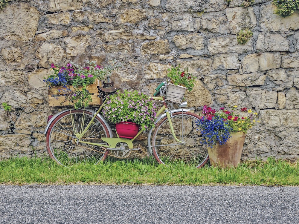 a bicycle with flowers in the basket parked next to a stone wall