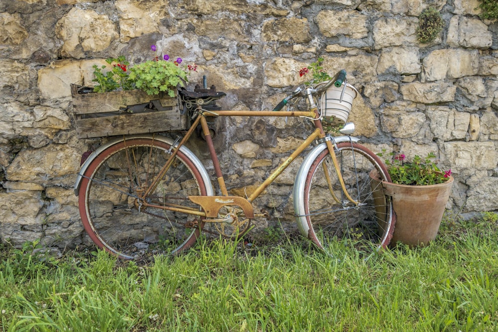 an old bicycle with a basket of flowers next to a stone wall