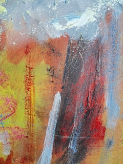 An abstract painting featuring a blend of vibrant colors and textured brushstrokes. The composition includes patches of red, yellow, blue, and white, with a mix of both bold and subtle movements. The paint appears layered, with visible streaks and splatters creating a dynamic and spontaneous pattern.