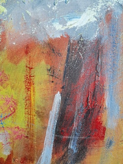 An abstract painting featuring a blend of vibrant colors and textured brushstrokes. The composition includes patches of red, yellow, blue, and white, with a mix of both bold and subtle movements. The paint appears layered, with visible streaks and splatters creating a dynamic and spontaneous pattern.