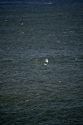 A vast expanse of water with small waves and ripples. Two people are engaged in water sports, likely windsurfing or kiteboarding, each using a board with a sail.