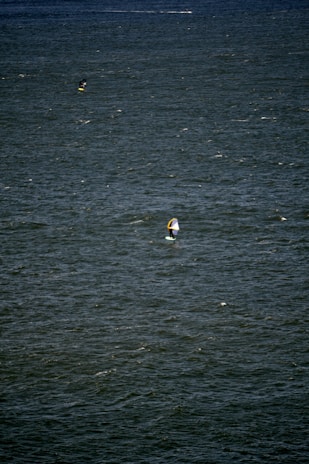 A vast expanse of water with small waves and ripples. Two people are engaged in water sports, likely windsurfing or kiteboarding, each using a board with a sail.