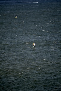 A vast expanse of water with small waves and ripples. Two people are engaged in water sports, likely windsurfing or kiteboarding, each using a board with a sail.