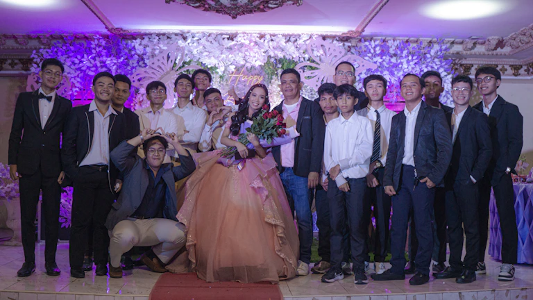 A joyful group photo of María José with her chambelanes under warm golden lights.
