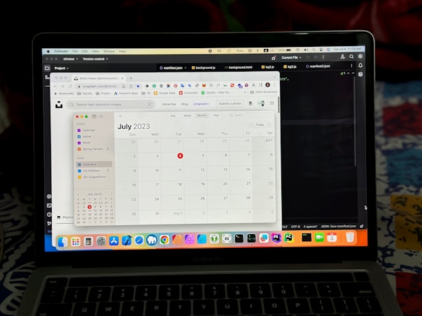 A MacBook Pro screen displaying a calendar application showing the month of July 2023. Visible tabs in the browser include website links and various project files, with some text editors or development environments open. The desktop background is partially visible, colored in dark tones.