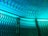 Intricate patterns of light and shadow cast on a textured surface, creating a rippling effect. A metallic mesh structure is positioned at an angle in the foreground, its hexagonal openings allowing light to filter through, resulting in a dynamic interplay of colors and forms.