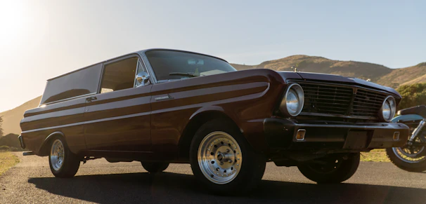 Side profile of a classic 1960s coupe restored to glossy black with gold-accented rims parked against Mallorca's sunlit coastline