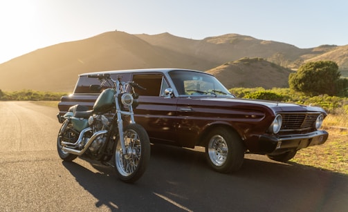 A vintage racing car and a motocross bike side by side under a sunset sky.