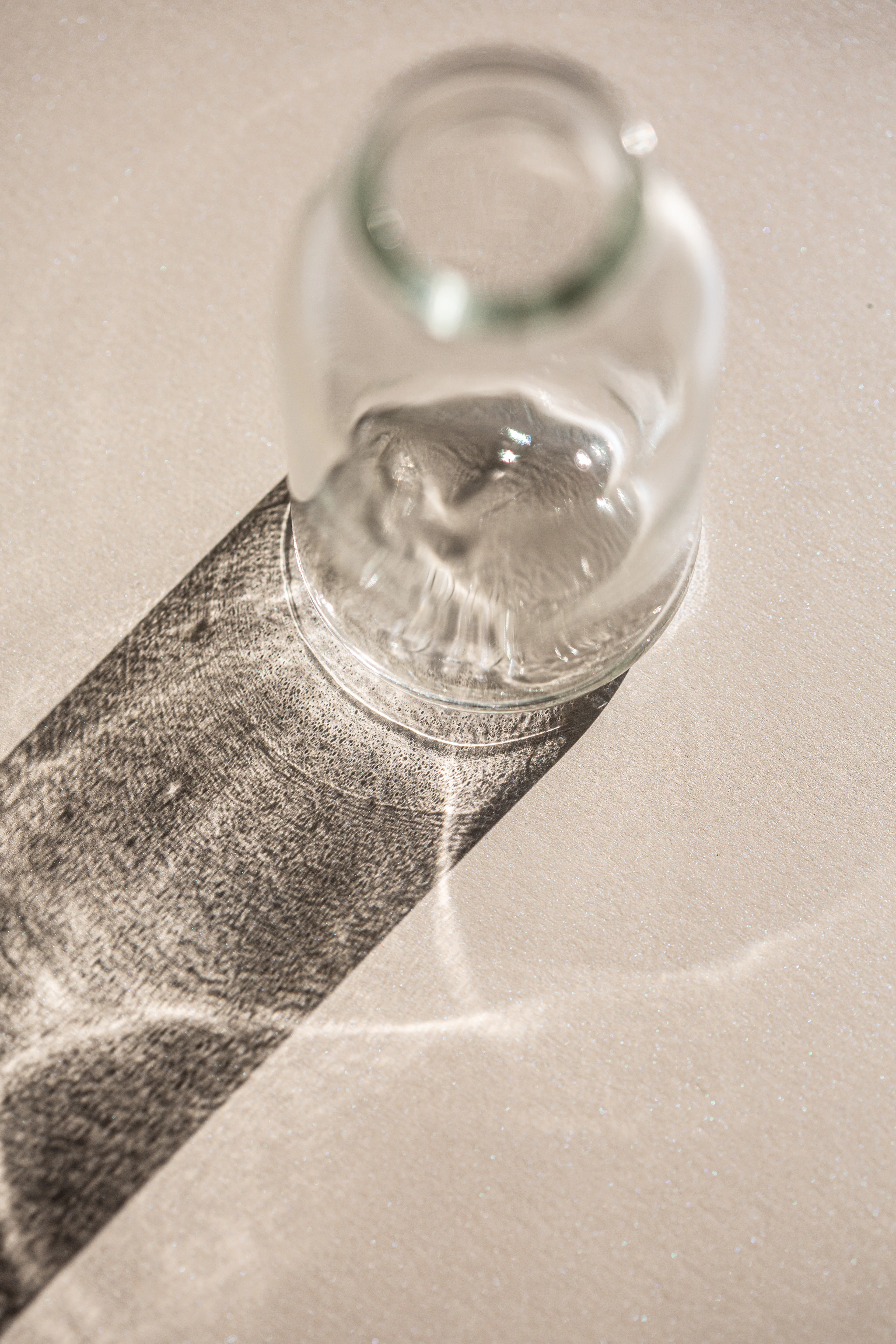Clear glass vessel on a warm beige surface, with a raking band of sunlight throwing a shimmering caustic shadow