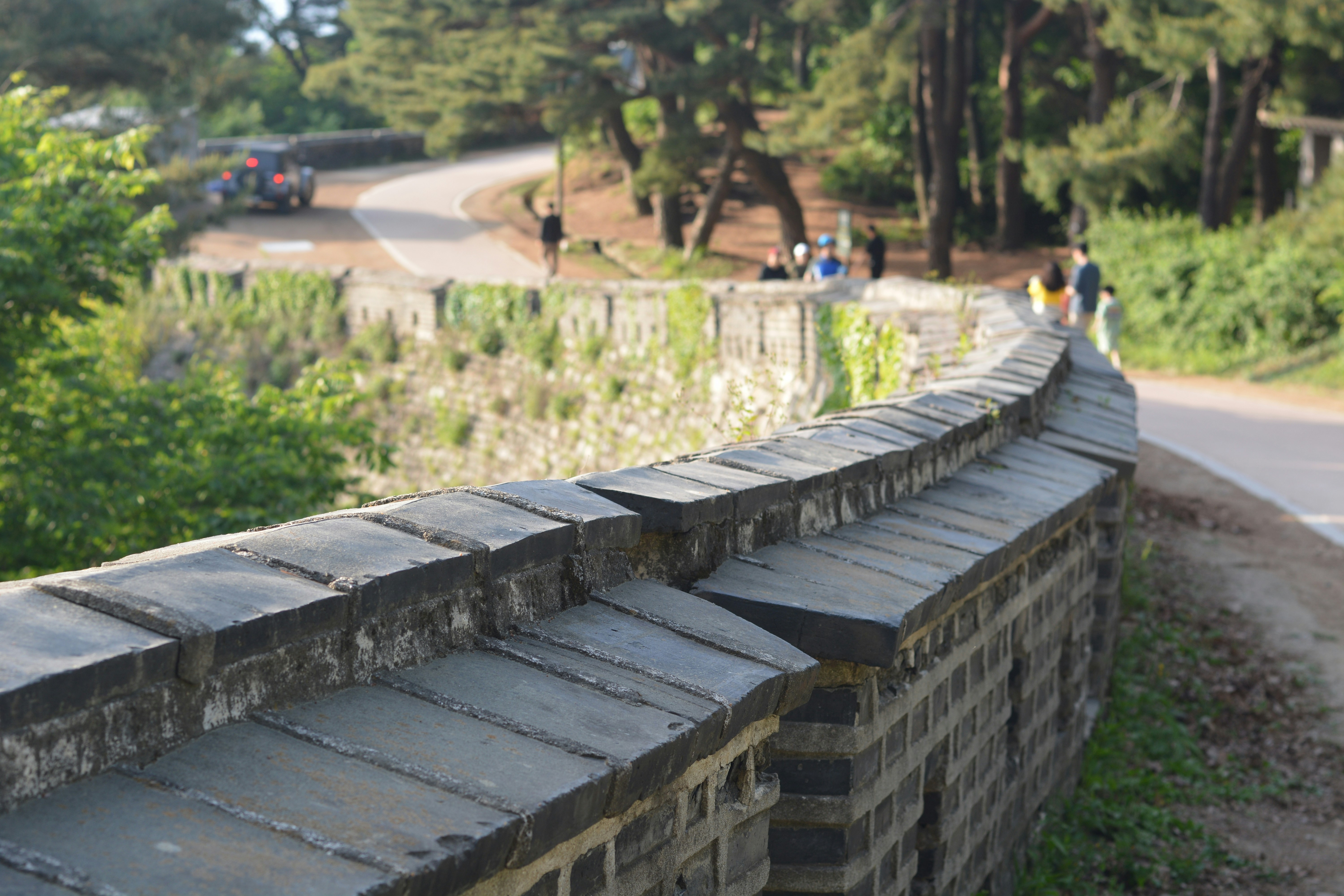 un muro de piedra cerca de una carretera con gente caminando sobre ella