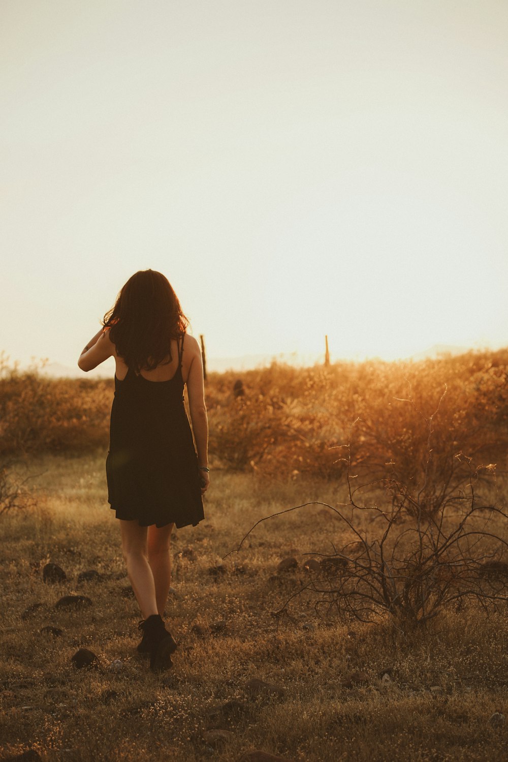 a woman in a black dress walking through a field