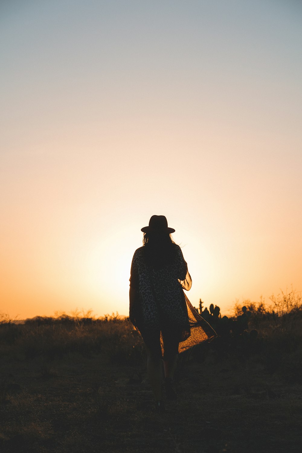 a woman walking through a field at sunset
