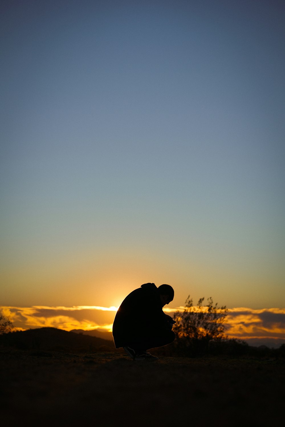 a silhouette of a person sitting on a hill at sunset