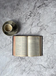 An open book beside a cup of tea on a minimalist black marble table with soft natural light.