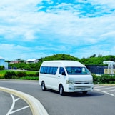 a white van driving down a street next to a lush green hillside