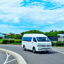 a white van driving down a street next to a lush green hillside