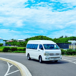 a white van driving down a street next to a lush green hillside