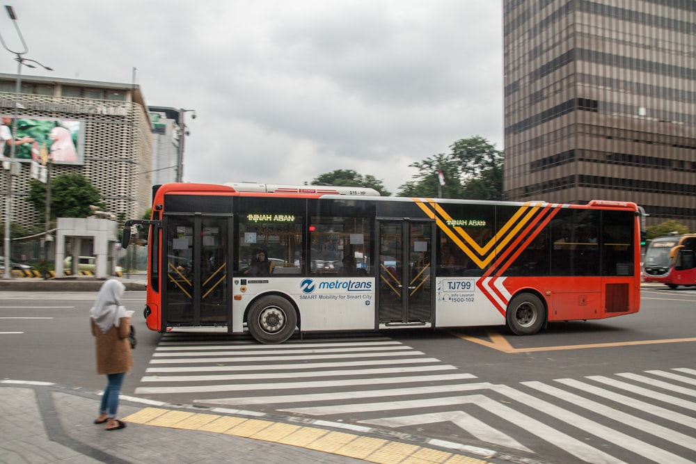 a red and white bus driving down a street next to tall buildings